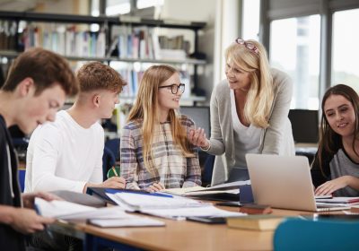 Female Teacher Working With College Students In Library