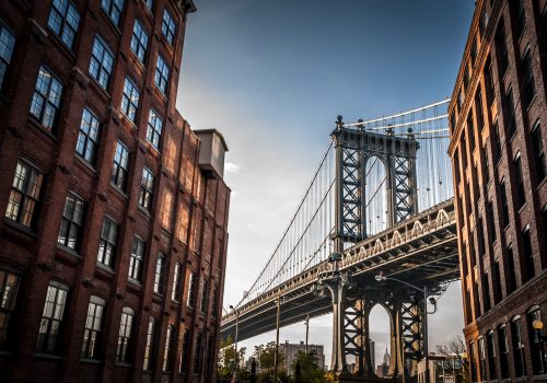 Manhattan bridge seen from a narrow alley enclosed by two brick buildings on a sunny day in summer
